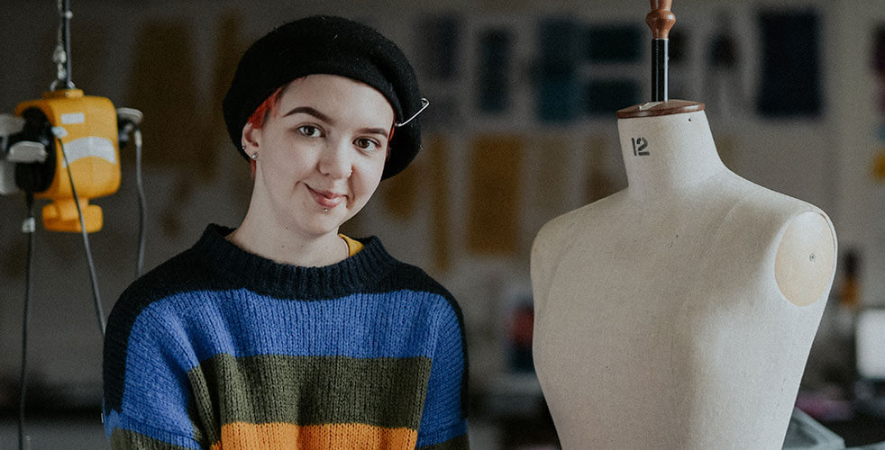 Student smiling facing the camera, beside a seamstress body dummy