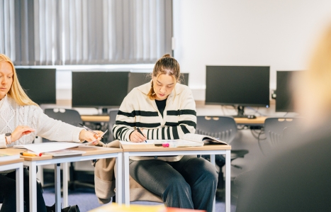 Student in a classroom at a desk looking down at their work