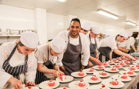 Michael Caines smiling at the camera with students around him working on dishes