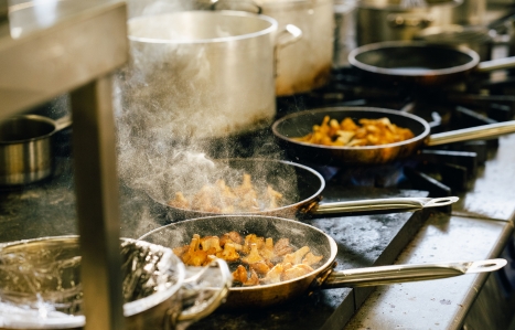 a line of frying pans on an oven with food cooking in them and steam rising