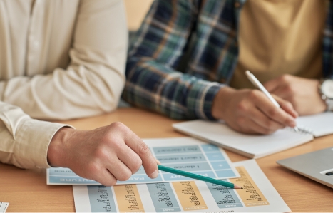 focus on hands holding a pencil on a desk with a student in the background holding a pen