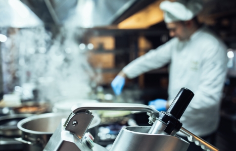 focus on kitchen equipment with a chef stirring something in the background