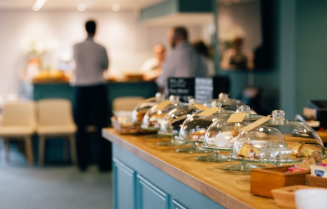 a cafe counter with pastries and cakes under domes and staff in the background