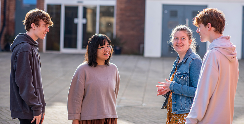 Four students stood outside on campus talking to each other smiling 