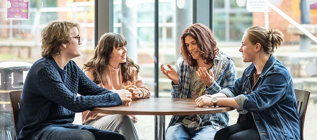 Group of four students sat at a table inside chatting