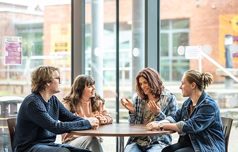 Group of four students sat at a table inside chatting