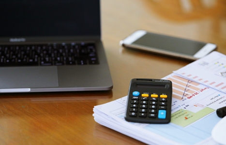 a laptop, calculator and some finance papers on a desk with a phone in the background