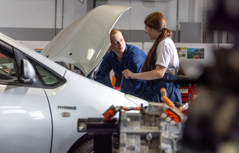 A car with it's bonnet open and two students looking into it