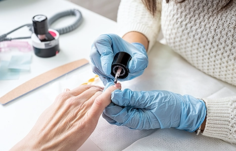 Nails being worked on by a person wearing blue plastic gloves