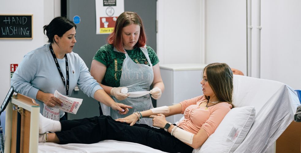 A student and teacher going over how to correctly apply a bandage on to a patients arm