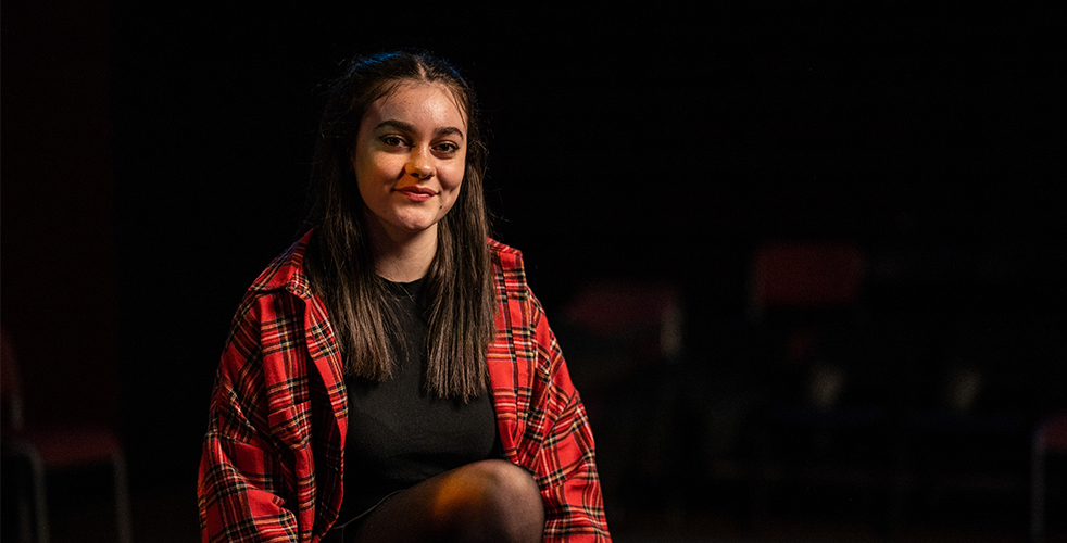 Female Student portrait smiling at the camera wearing a black top and red checked jacket