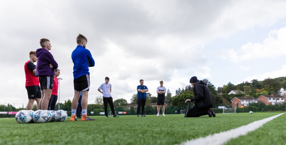 Sports students on a pitch looking at a coach