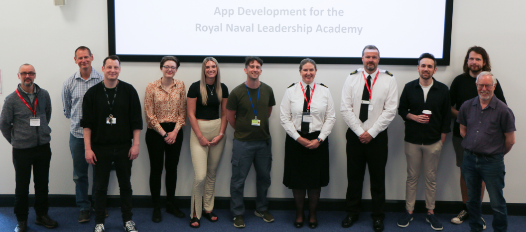 Group of staff and royal navy staff stood smiling at the camera