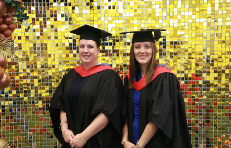 Two students smile at the camera in graduation gowns