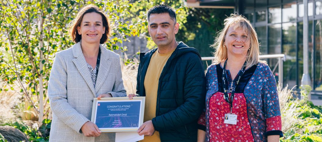 A certificate is presented to a male adult learner outside in the sun.