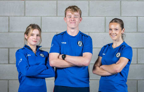 Two female and one male sport students smile at the camera in their blue academy kit.