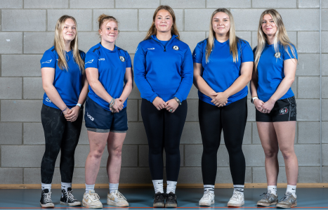 Five female rugby players smile at the camera in their blue academy kit.