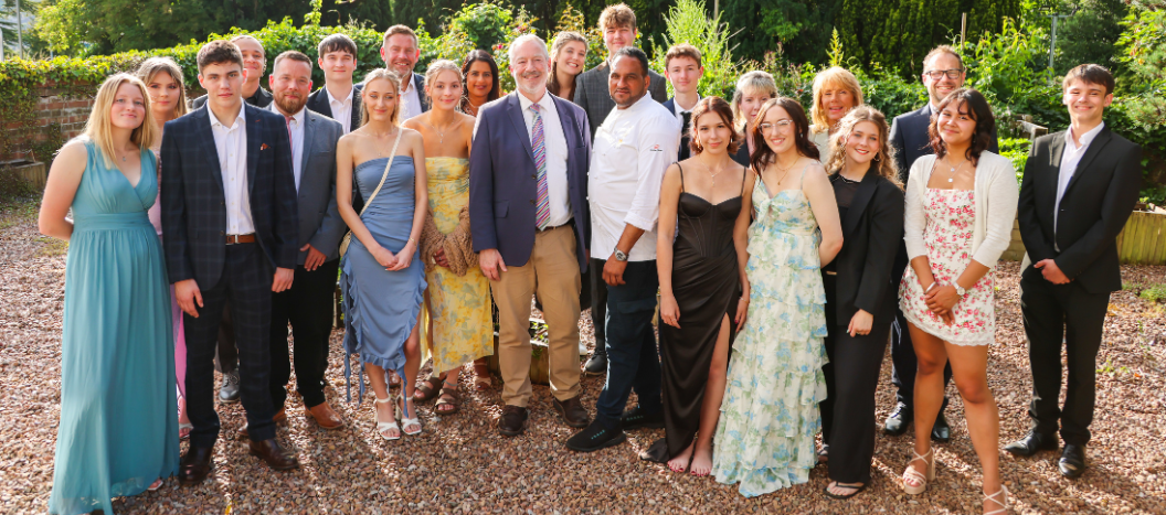 The graduating class of 2024 stand in the herb garden in dresses and suits