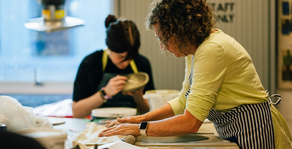 Two adult learners in a pottery class working on their pieces