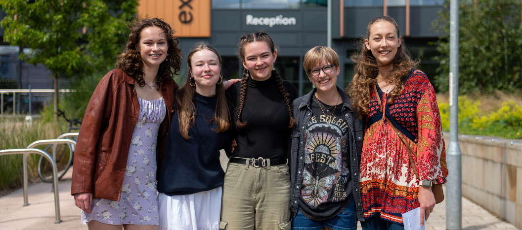 Students collecting their IB results stand in front of the college hugging one another.