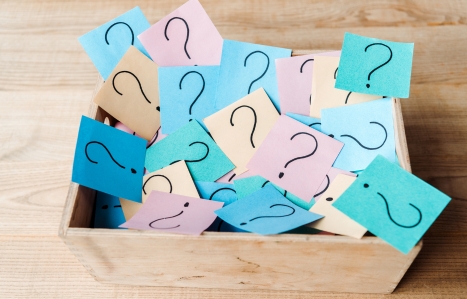 overhead view of sticky notes with question marks in wooden box on desk