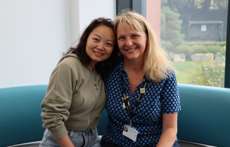 An adult learner and tutor embrace and smile at the camera.