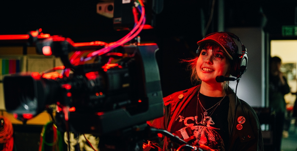 A student with headphones using camera filming equipment in the TV studio