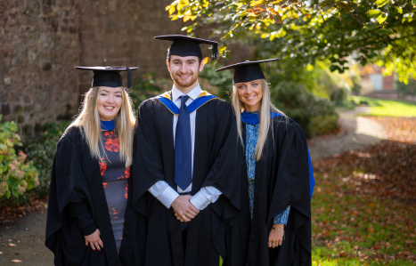 A group of graduates stand outside and smile at the camera