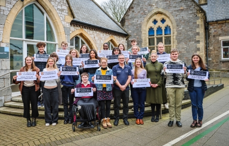 A large group of students smiling at the camera holding a sign stating which uni they have been accepted for