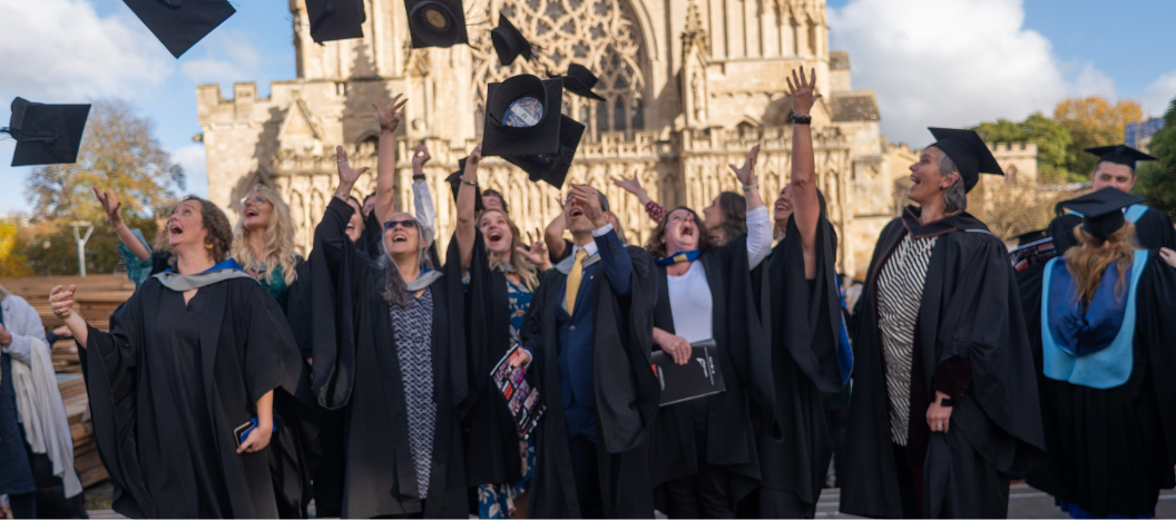 A group of graduates throw their caps in the air outside Exeter Cathedral.