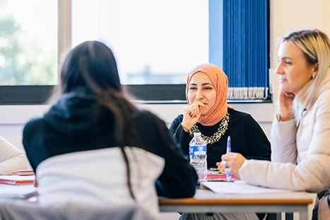 Three people sat in a classroom smiling and talking