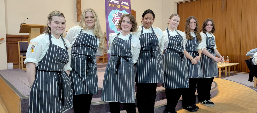 Student chefs stand on stage in their aprons.