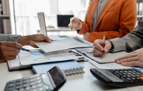 Focus on the hands of three people sat at a desk with calculators and accountancy paperwork.