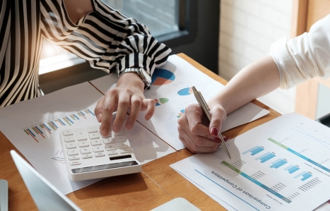 Focus on the arms of two people looking at accountancy paperwork with a calculator.