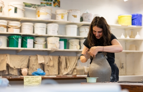 student with a large pot in a pottery studio