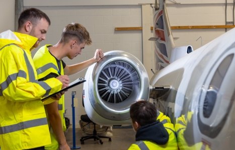 Three male students in aircraft engineering hangar looking at aircraft engine