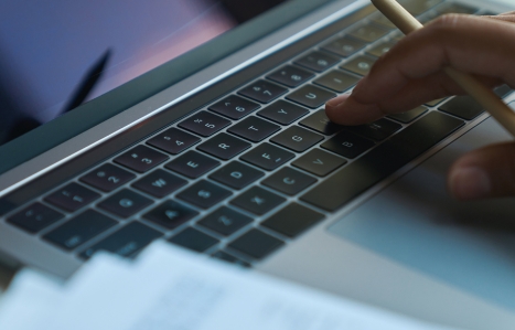 hand with pencil typing on a laptop