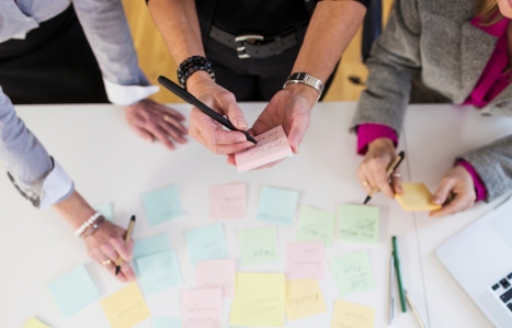 Focus on the hands of three people with pens and post it notes