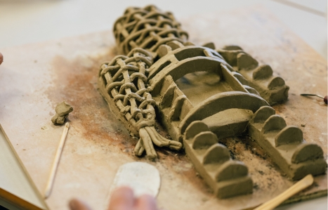 A working clay sculpture of an intricately woven man or robot figure