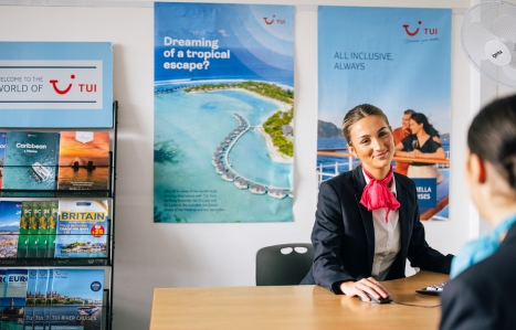 student smiling at another student in uniform sat at a desk with tui travel and tourism posters behind them
