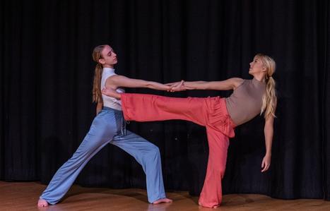 two studnets dancing togethrr with one girl with both her leg and arm out to the sdie balancing on one foot and the second girl is catching the arm of the first
