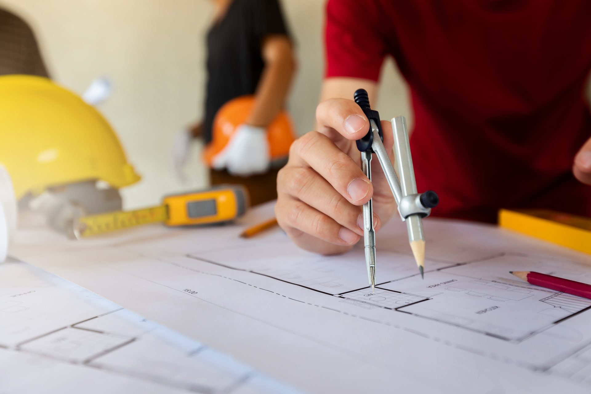 An architect or engineer uses a divider gauge on the blueprint.