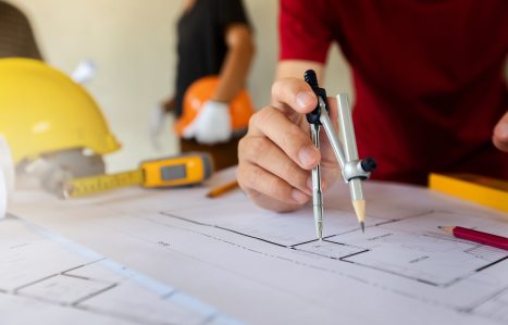 An architect or engineer uses a divider gauge on the blueprint.