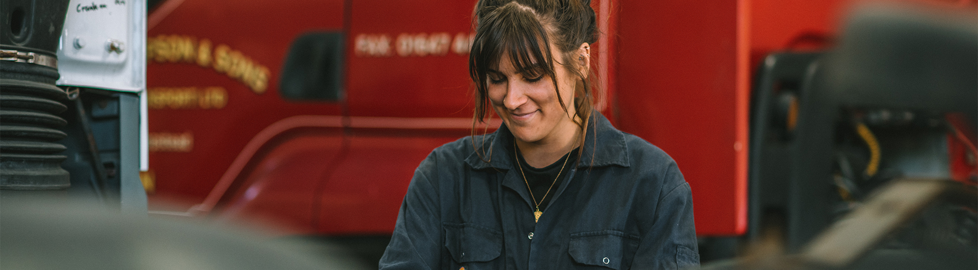 female adult learner in boiler suit in automotive workshop