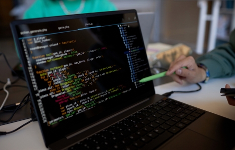 Focus on laptop screen with coded data and pen held by hand