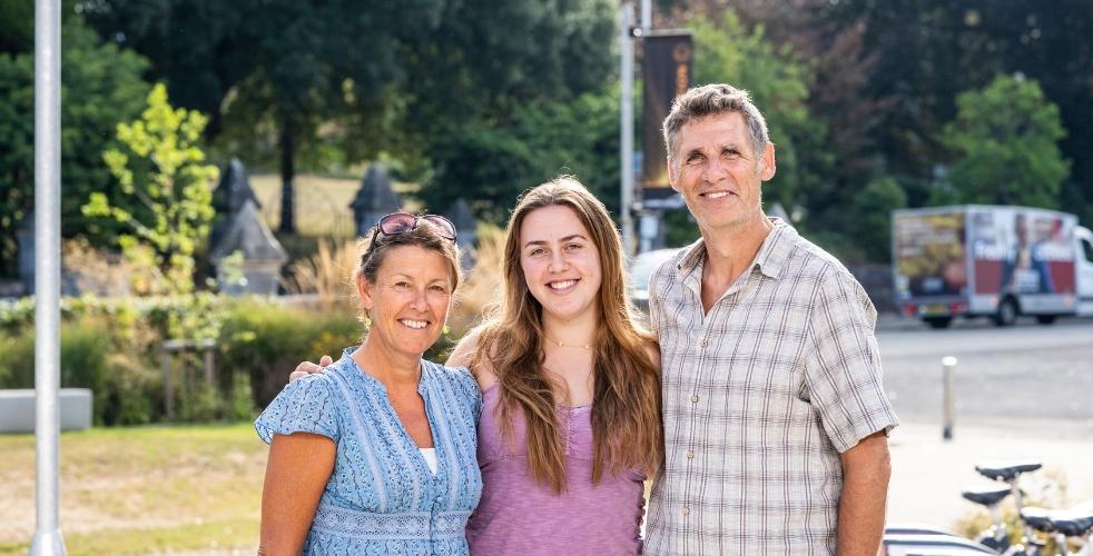 Student stood with arms around their two parents