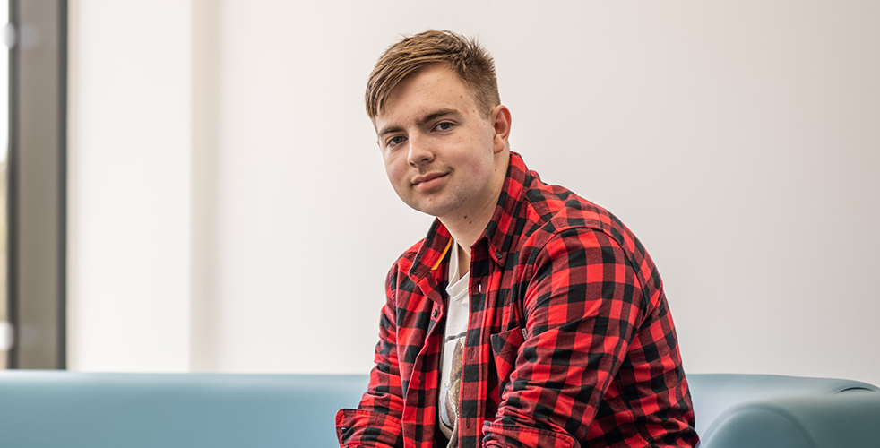 Male Student portrait smiling at the camera wearing a red and lack checked shirt