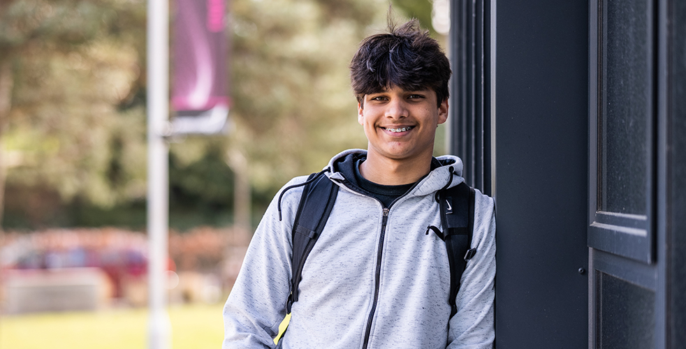 Male Student portrait smiling at the camera wearing a grey zipped hoodie