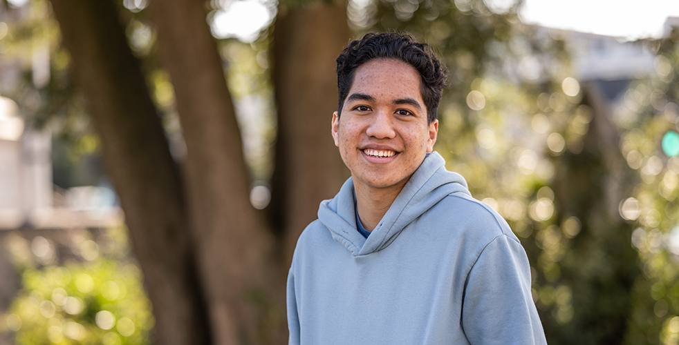 Male Student portrait smiling at the camera wearing a grey blue hoodie