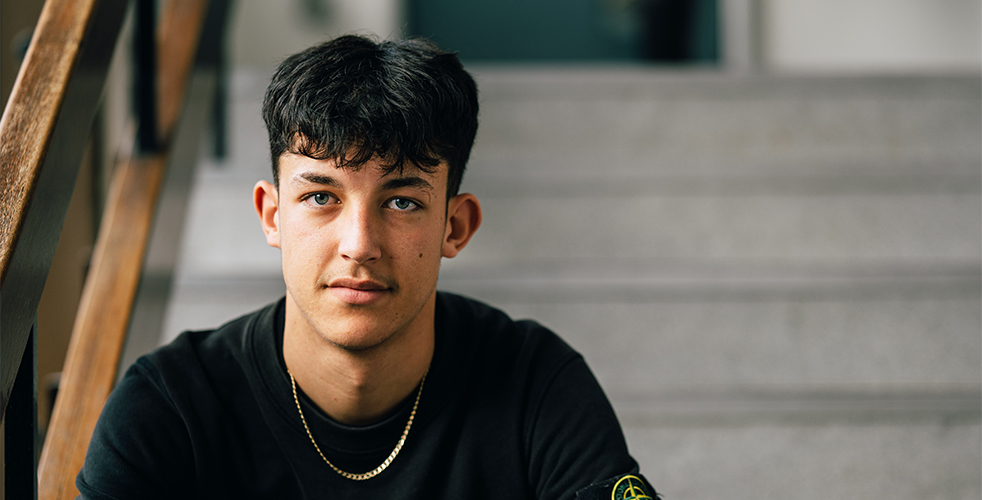 Male student portrait smiling at the camera sat on the steps in a black top